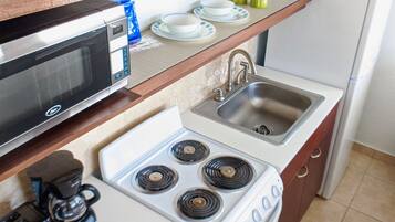 A compact kitchen with a microwave, stove, sink, and coffee maker.