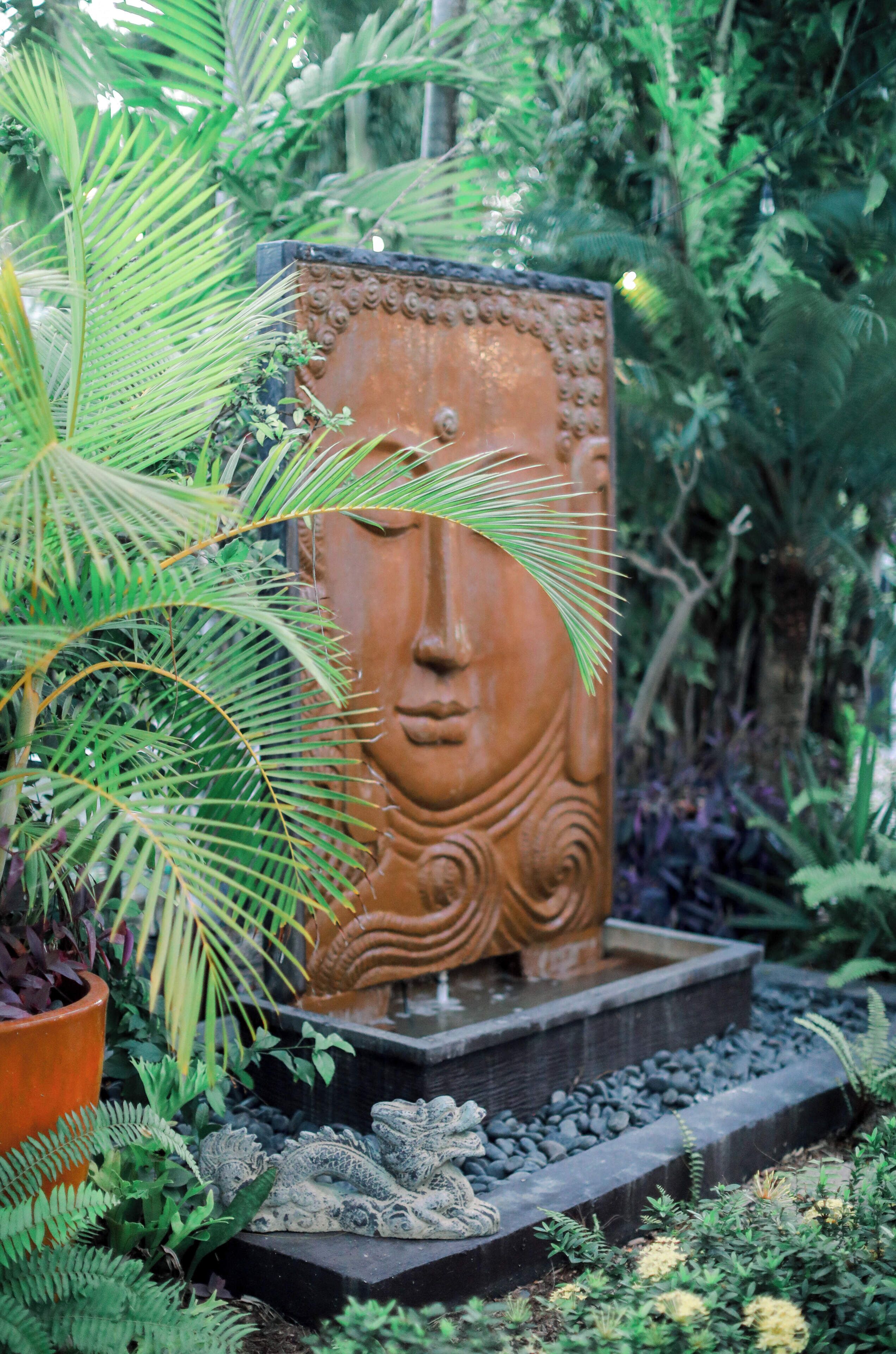 Un jardin agrémenté d’une sculpture centrale, entouré de différentes plantes et doté d’un sentier en pierre.