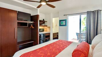 A bedroom with a bed, a ceiling fan, a wardrobe, a kitchenette, and a balcony with curtains.