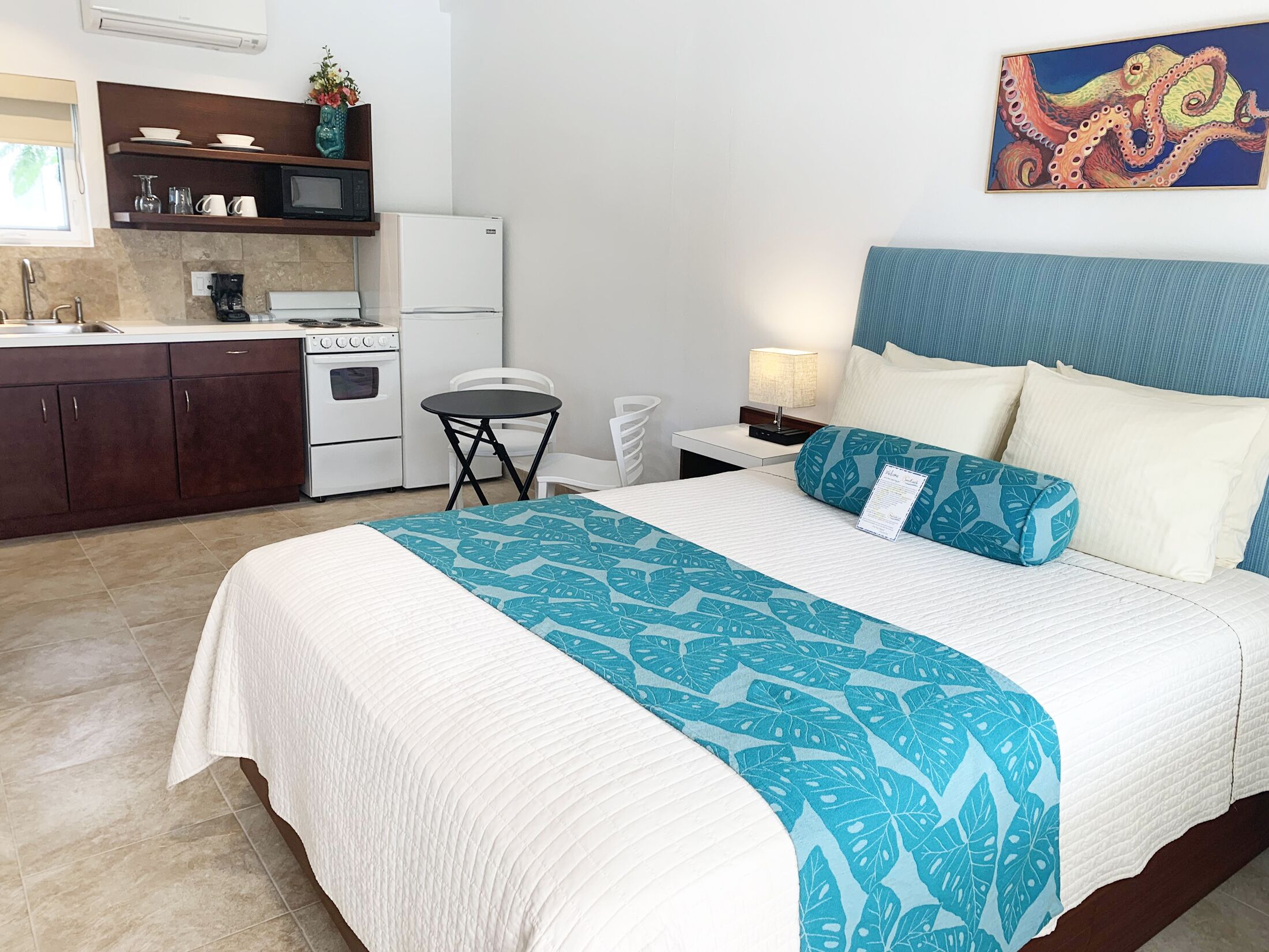 A hotel room with a bed, a small kitchenette, a dining area, and a bathroom.