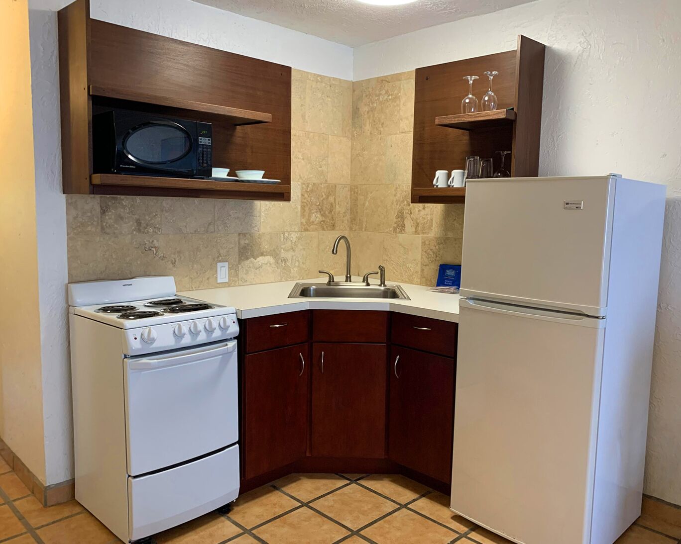 A compact kitchen with a stove, microwave, sink, and refrigerator.