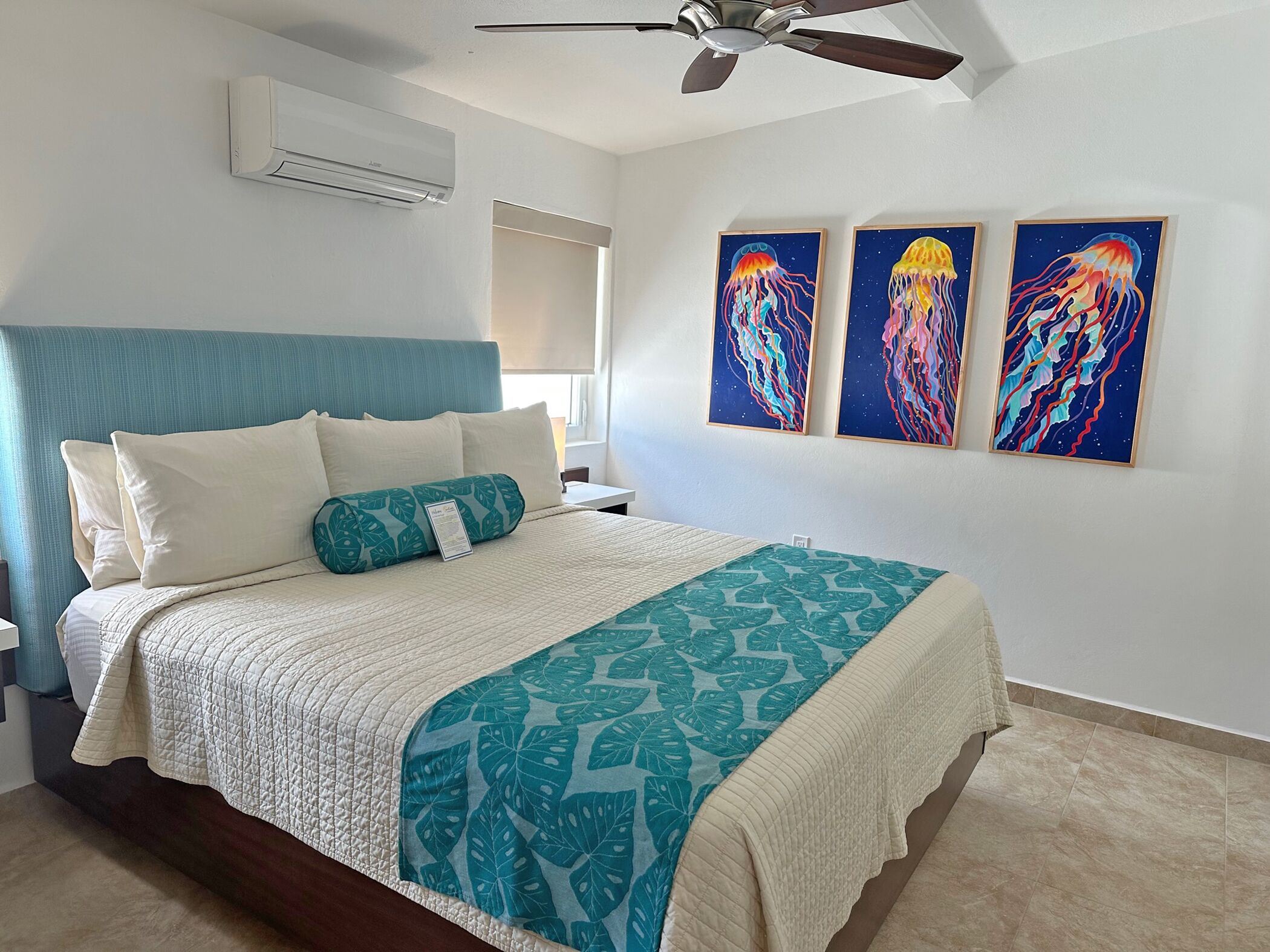 A bedroom with a bed, a ceiling fan, and three wall-mounted paintings.