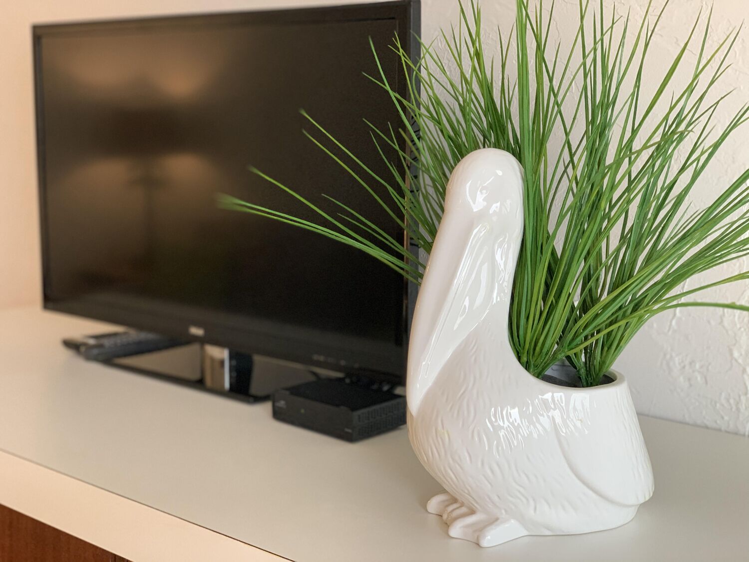 A white ceramic penguin-shaped planter with green grass on a white surface next to a flat-screen TV.