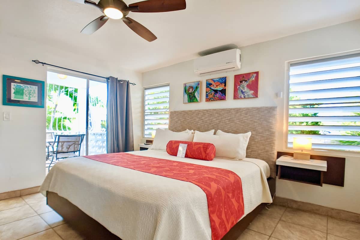 Habitación de hotel con cama, ventilador de techo, aire acondicionado, obras de arte y ventana con persianas.