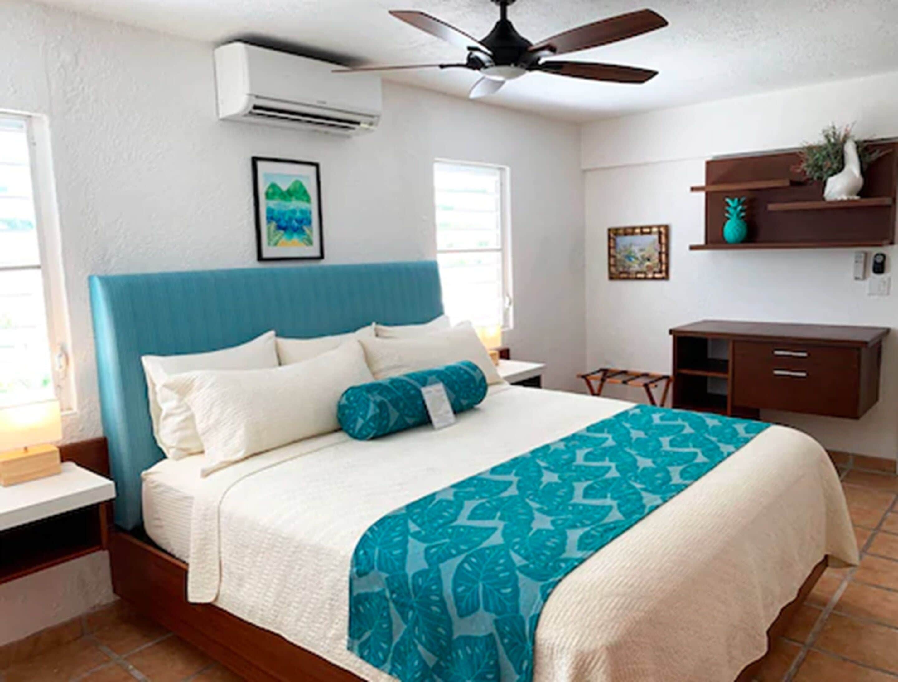 Une chambre à coucher comprenant un lit, un ventilateur de plafond, une table de chevet, un bureau et une étagère avec des objets décoratifs.