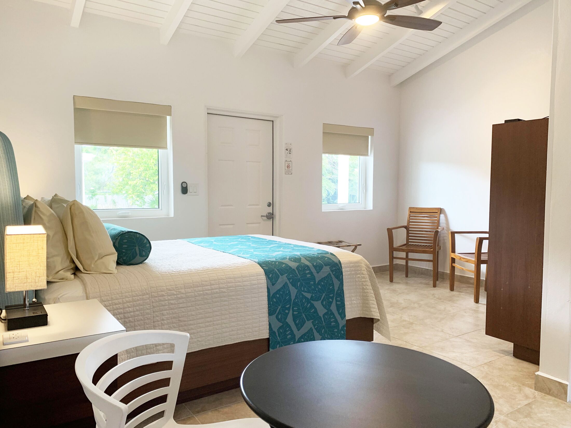 A bedroom with a bed, bedside table, lamp, chair, and a small table.