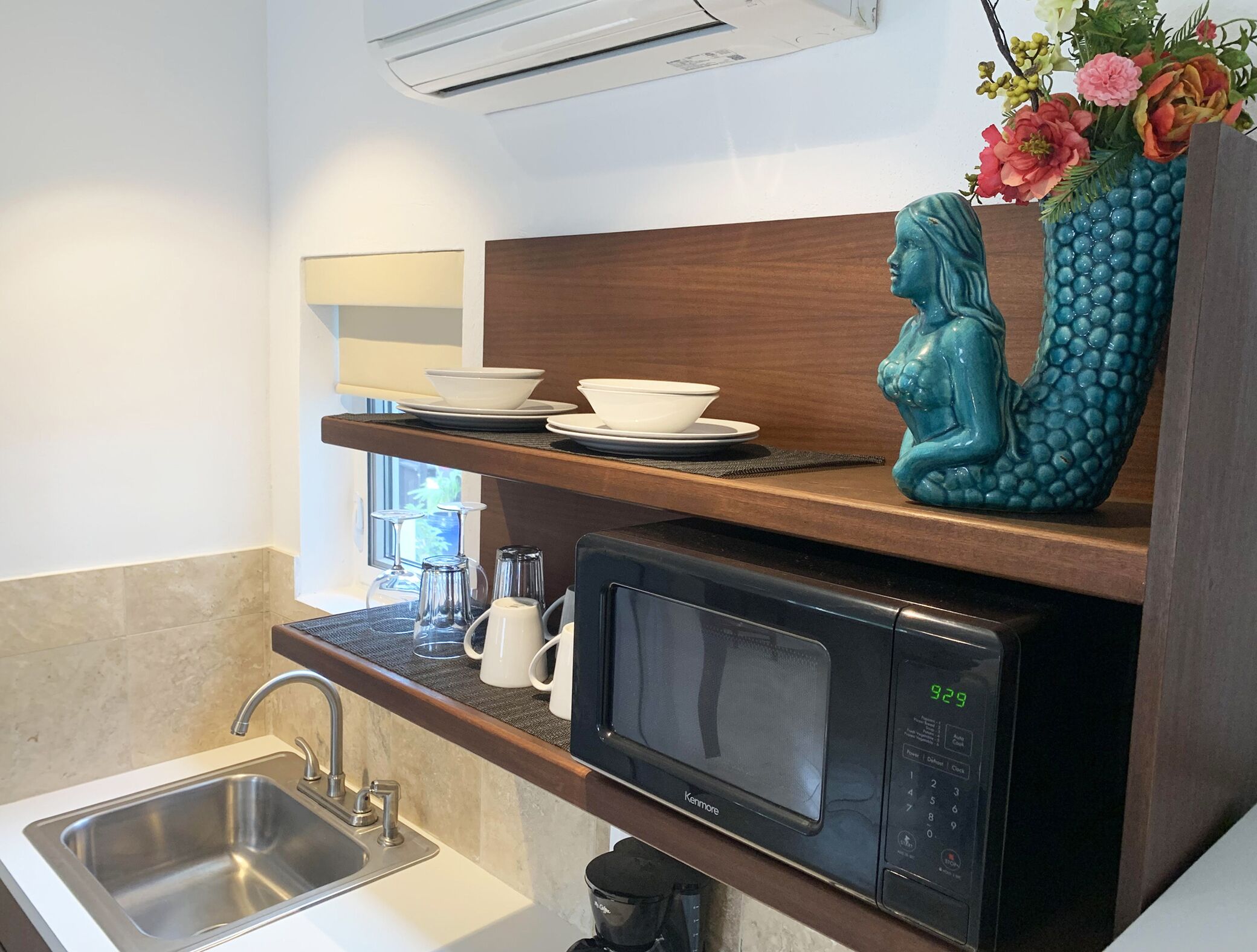 A modern kitchen with a Kenmore microwave, a sink, and a shelf with white bowls and a decorative blue vase.