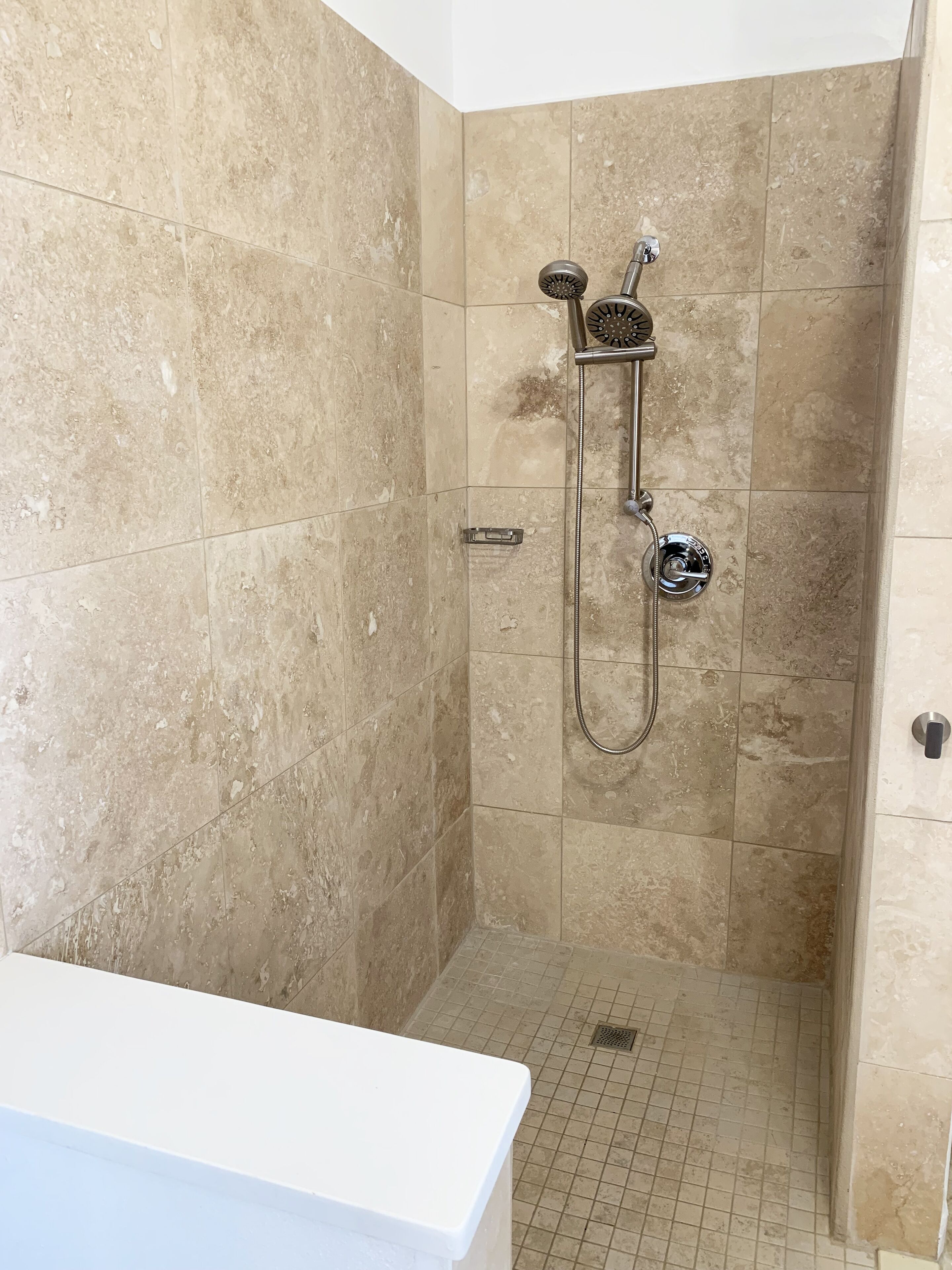 A small, tiled shower room with a single showerhead and a handheld shower attachment.