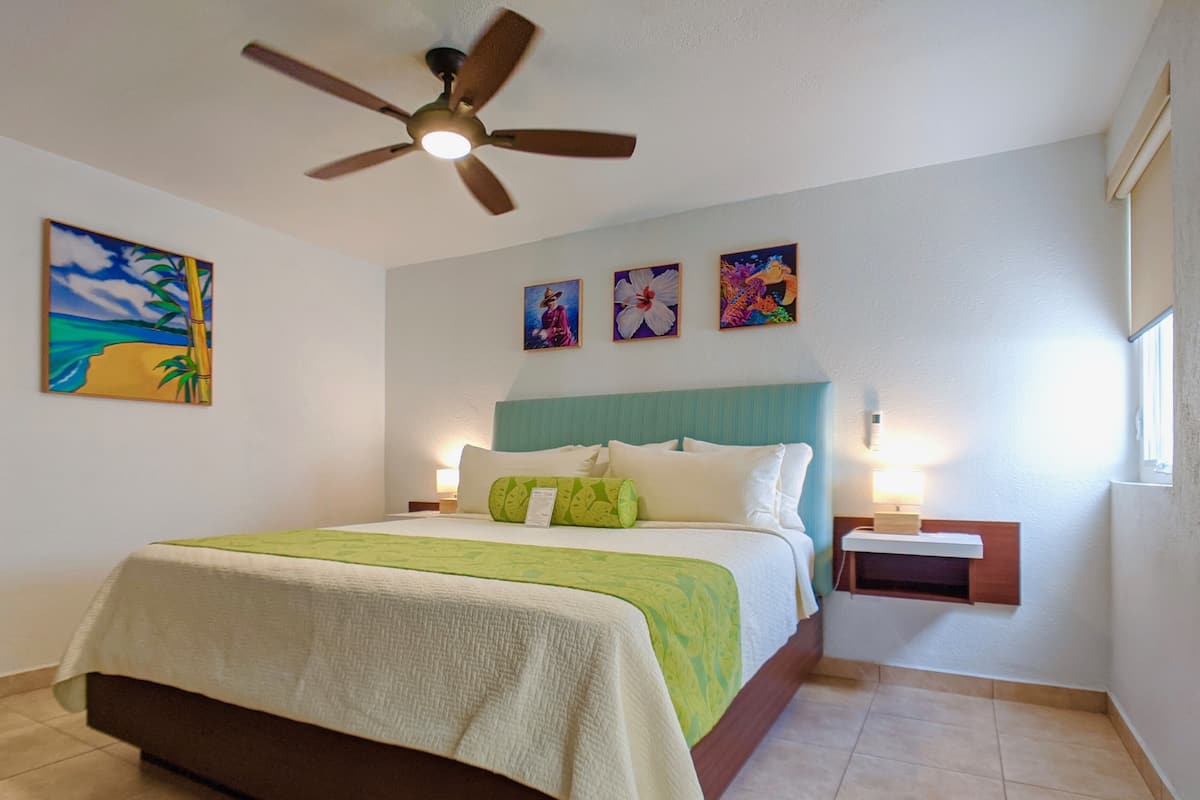 Habitación de hotel con cama, ventilador de techo y obras de arte en las paredes.