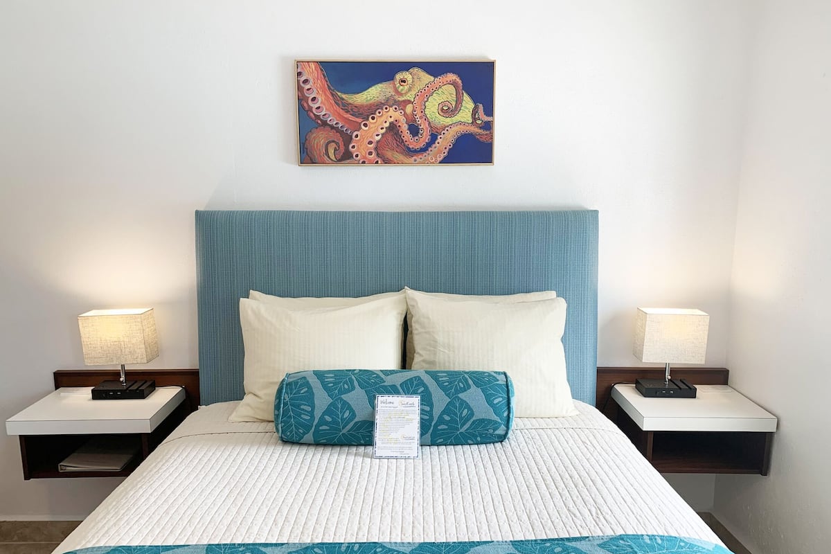 Habitación de hotel con una cama grande, dos mesitas de noche, cabecero y un cuadro de un pulpo en la pared.