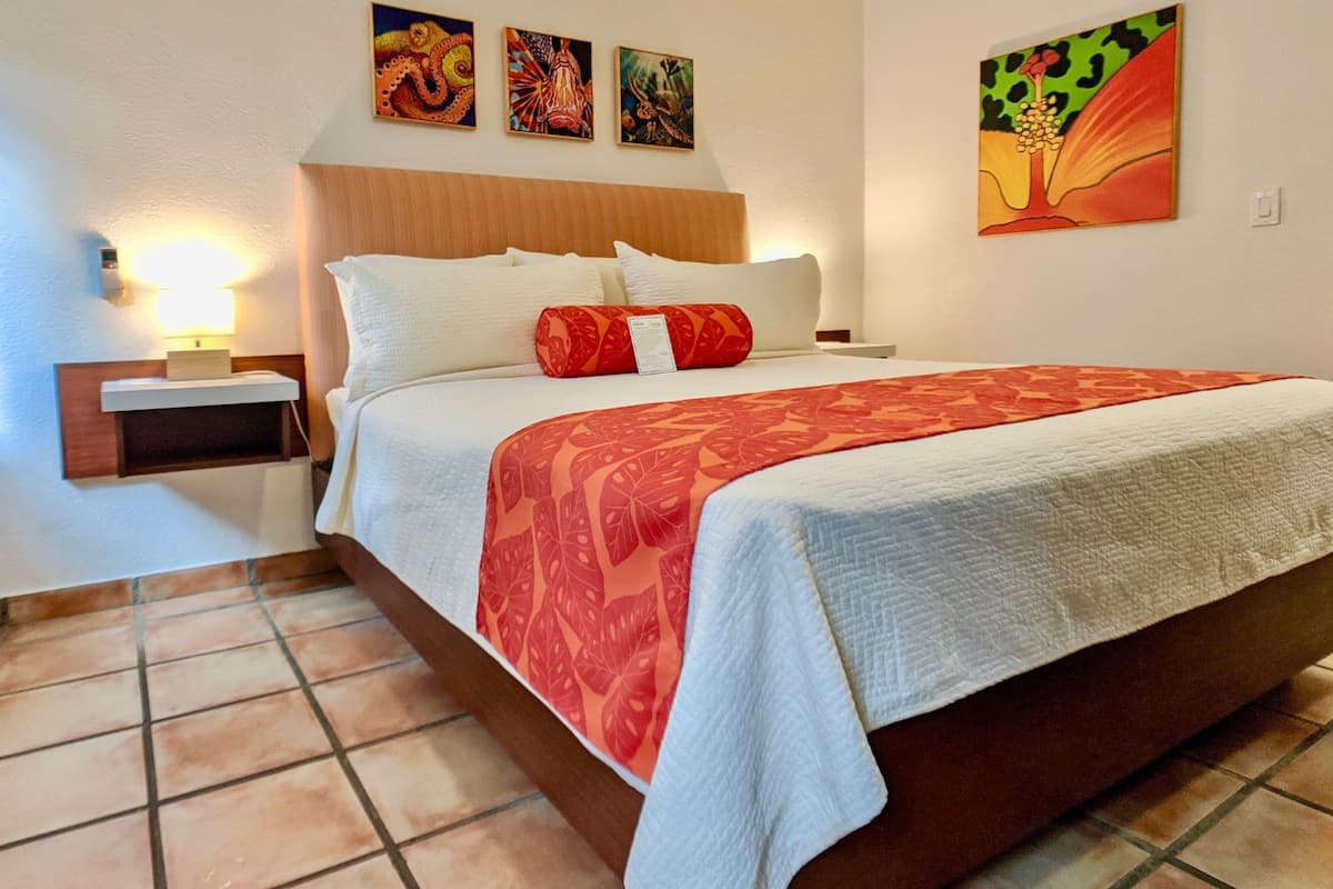 Habitación de hotel con una cama grande, una mesita de noche, una lámpara de pared y tres cuadros en la pared.