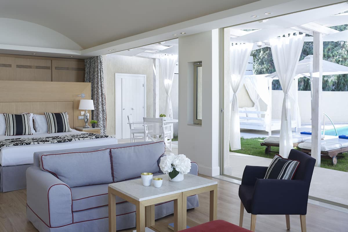 Ein modernes Hotelzimmer mit Bett, Sofa, einem kleinen Tisch mit Vase und Blick ins Freie.
