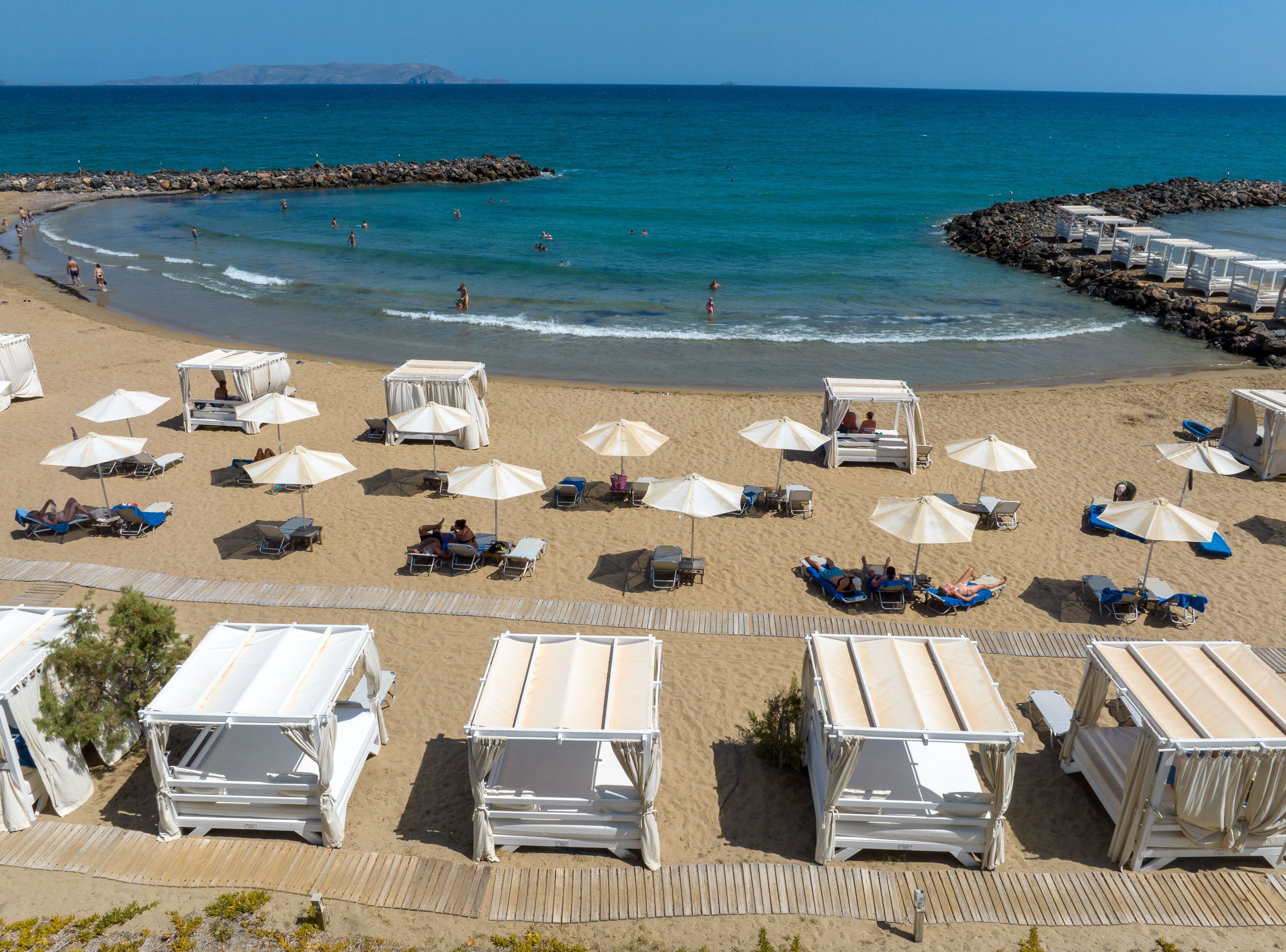 A beach with sun loungers, umbrellas, and beach huts.