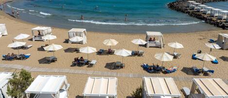A beach with sun loungers, umbrellas, and beach huts.