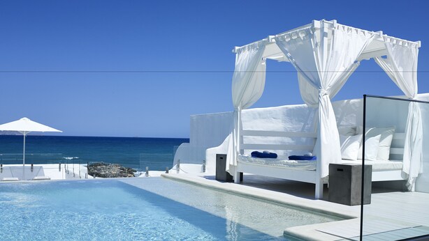 A poolside area with a white canopy bed, a lounge chair, and a view of the ocean.
