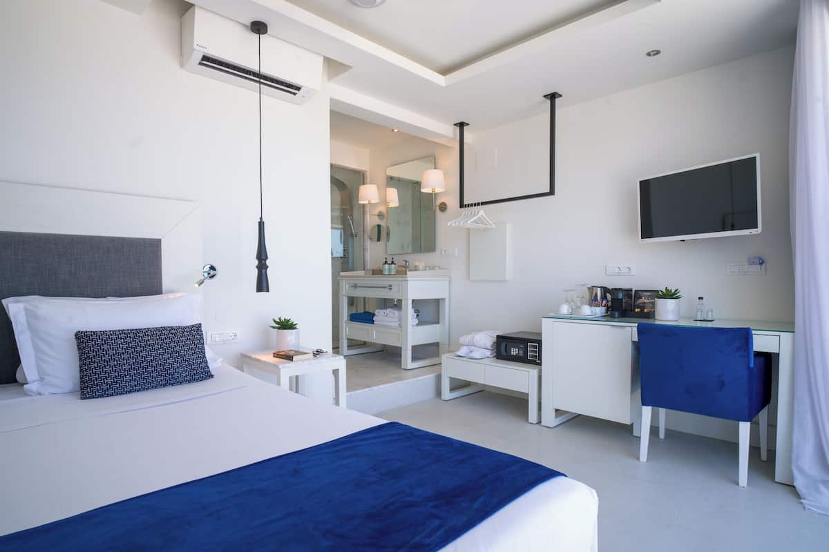Ein modernes Hotelzimmer mit einem großen Bett, einem Schreibtisch, einem Fernseher und einem durch eine geöffnete Tür einsehbaren Badezimmer.