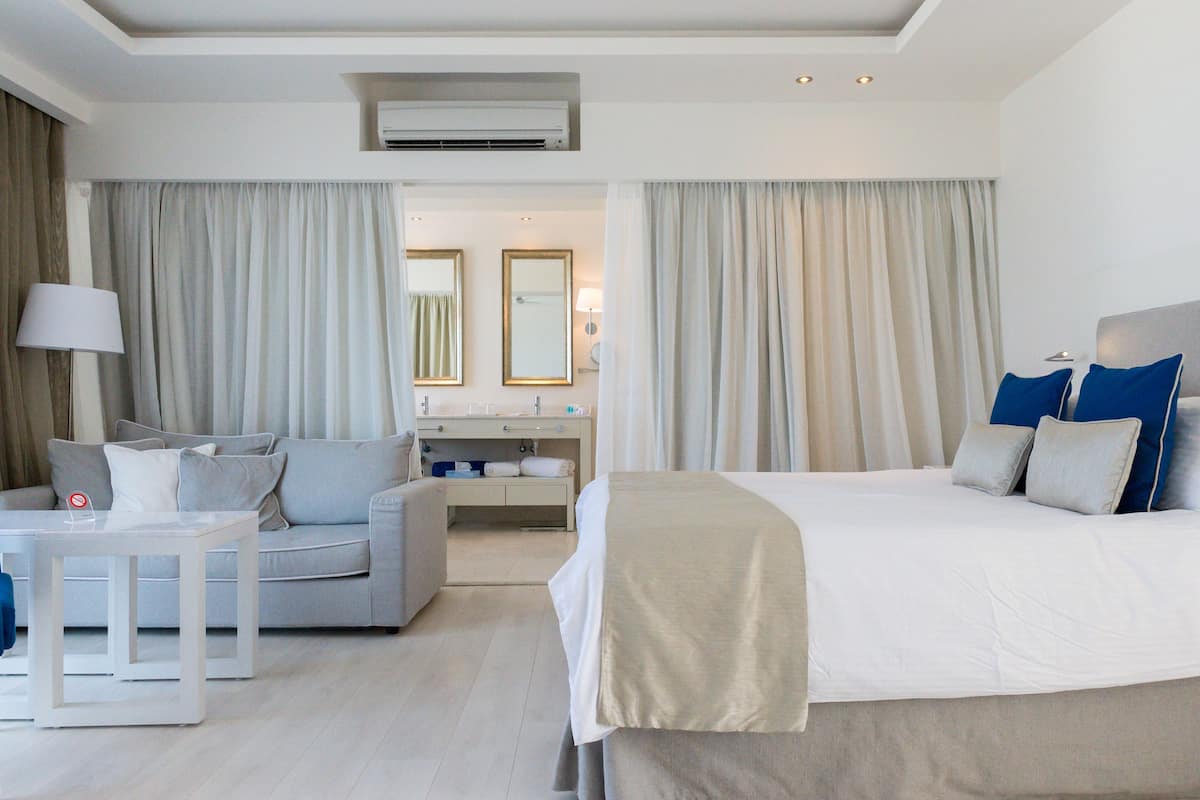 Ein Hotelzimmer mit Bett, Sofa, kleinem Tisch, Spiegel und einem durchgegangenen Tür erkennbaren Badezimmer.