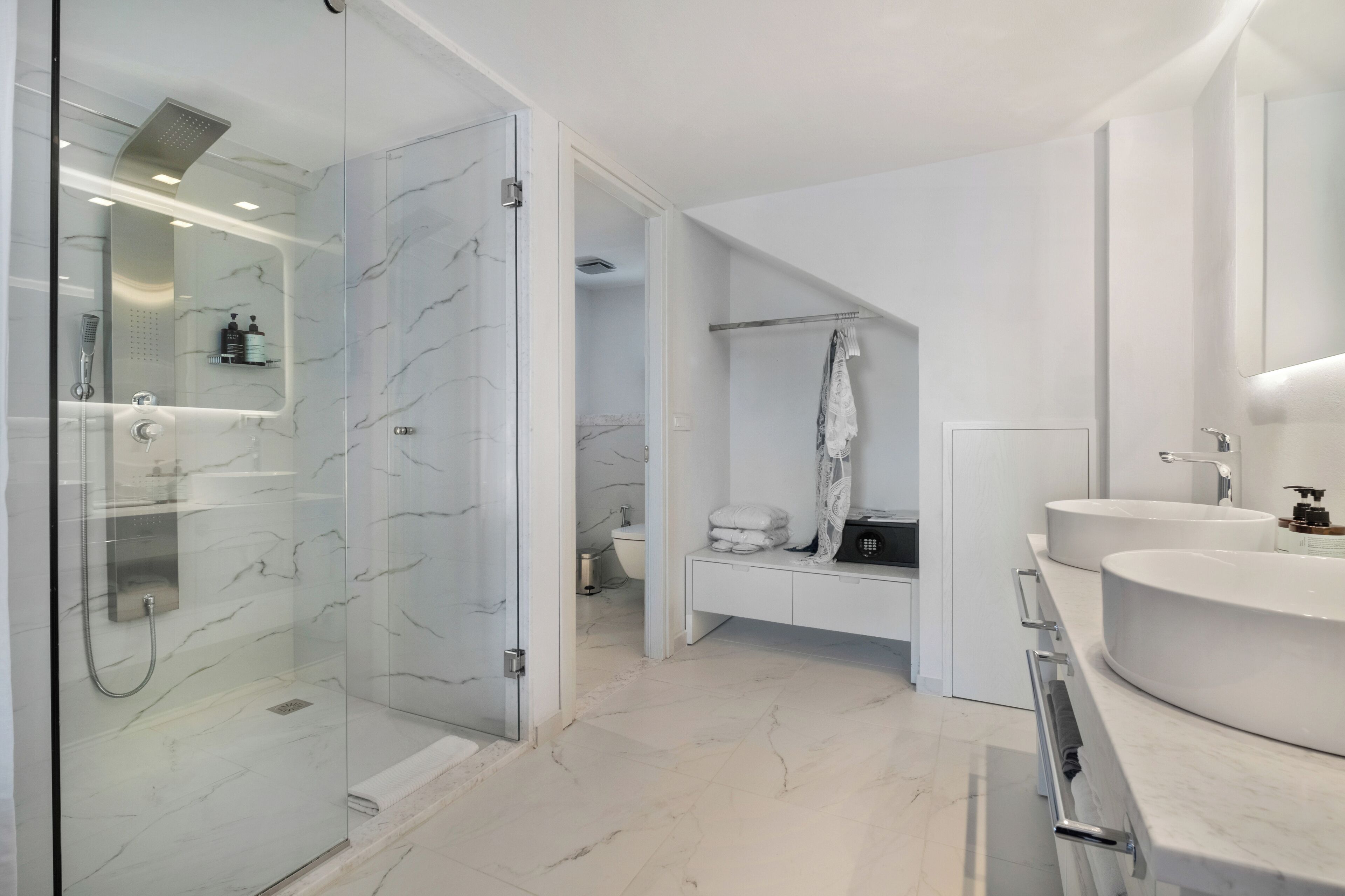 A modern bathroom with a glass-enclosed shower, a vanity with two sinks, and a walk-in closet.