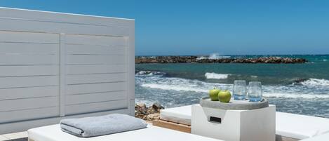 A sunlit room with a wooden deck, a white cushioned seating area, and a view of the ocean.