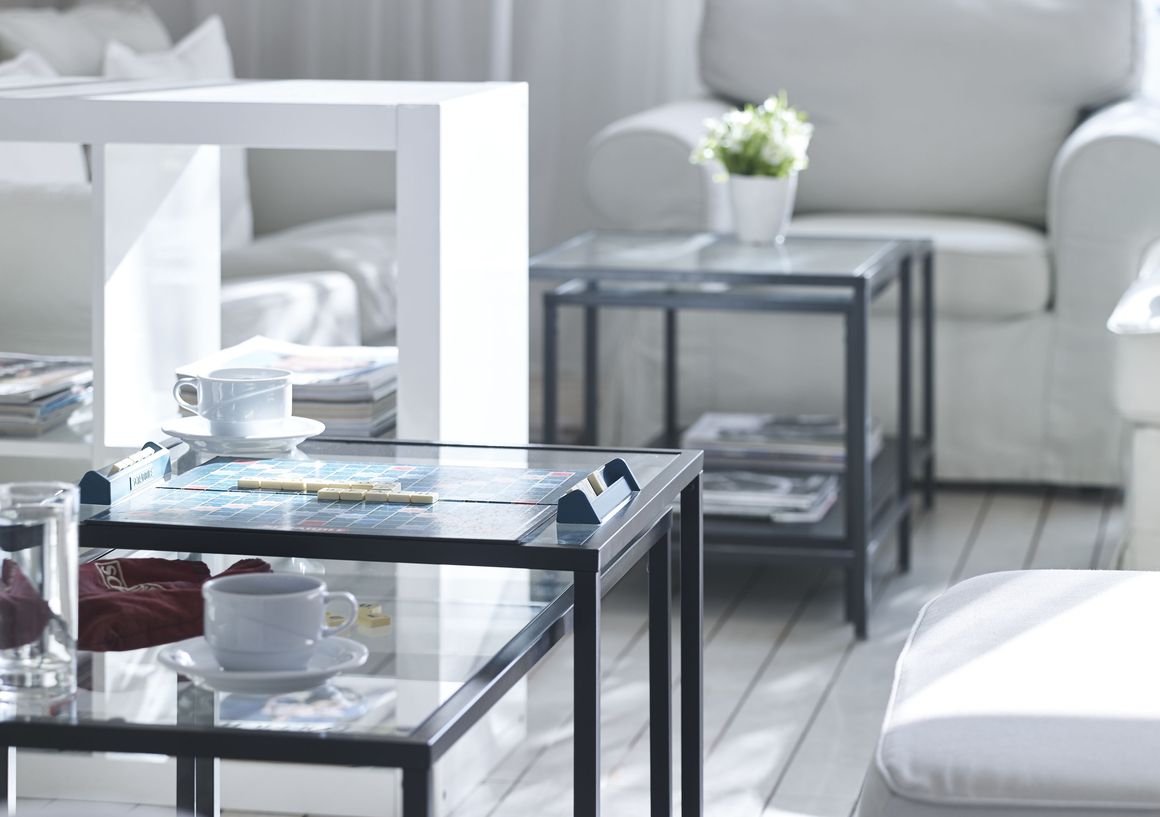 Una sala de estar moderna y minimalista con una mesa de centro de vidrio, sofás blancos y una pequeña mesa auxiliar con una planta.