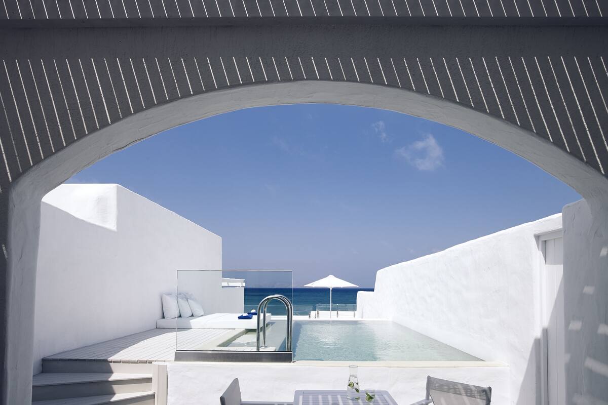 Ein moderner Poolbereich im Freien mit freiem Blick auf das Meer, einer gläsernen Lounge und einer Treppe, die zu einer erhöhten Ebene führt.