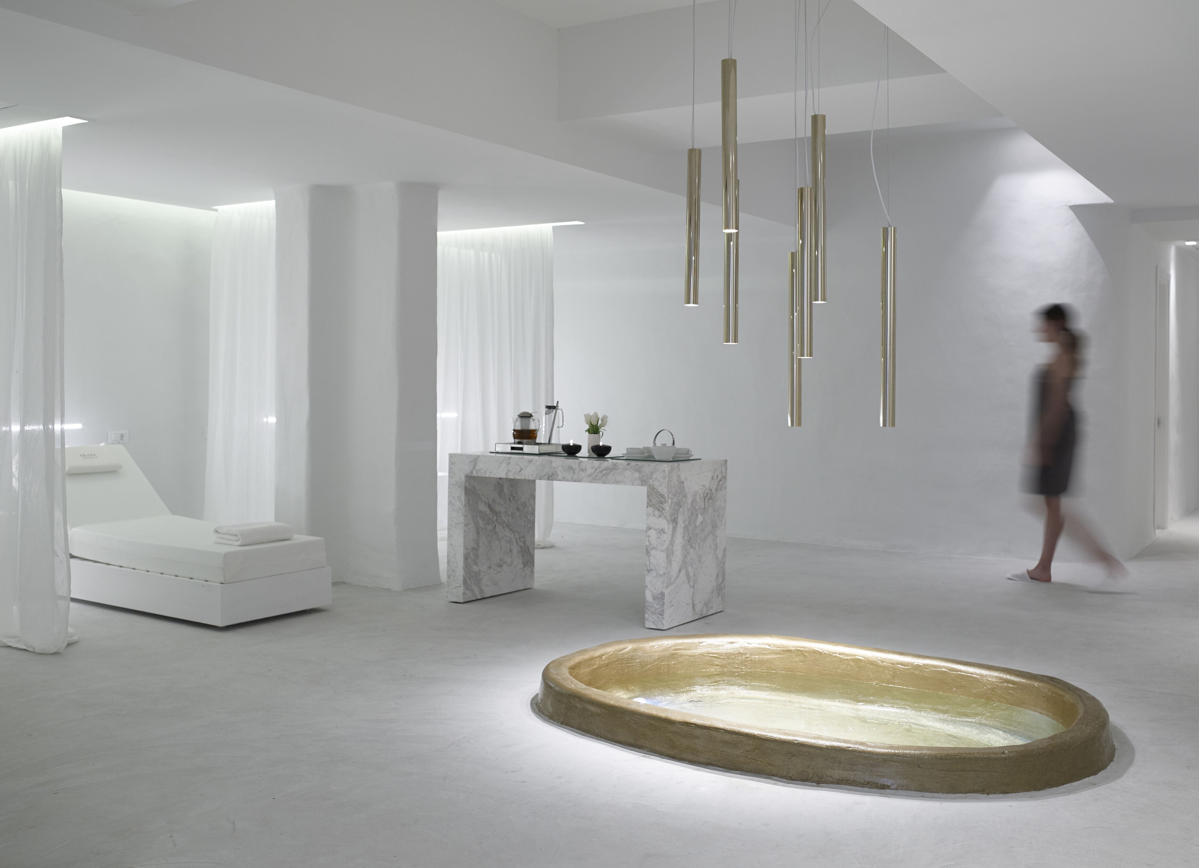 Een moderne, minimalistische badkamer met een marmeren wastafelmeubel, een groot bad en hanglampen.