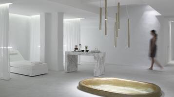 Un baño moderno y minimalista con tocador de mármol, una bañera grande e iluminación colgante.