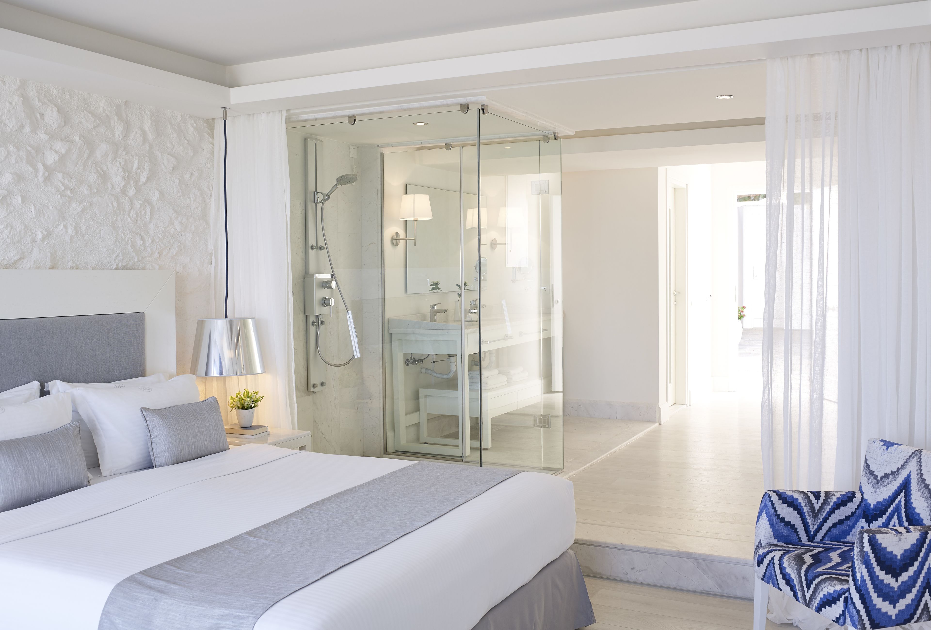 Ein modernes Hotelzimmer mit einem großen Bett, einer gläsernen Dusche, einem Badezimmer mit Spiegel und Blick ins Freie.