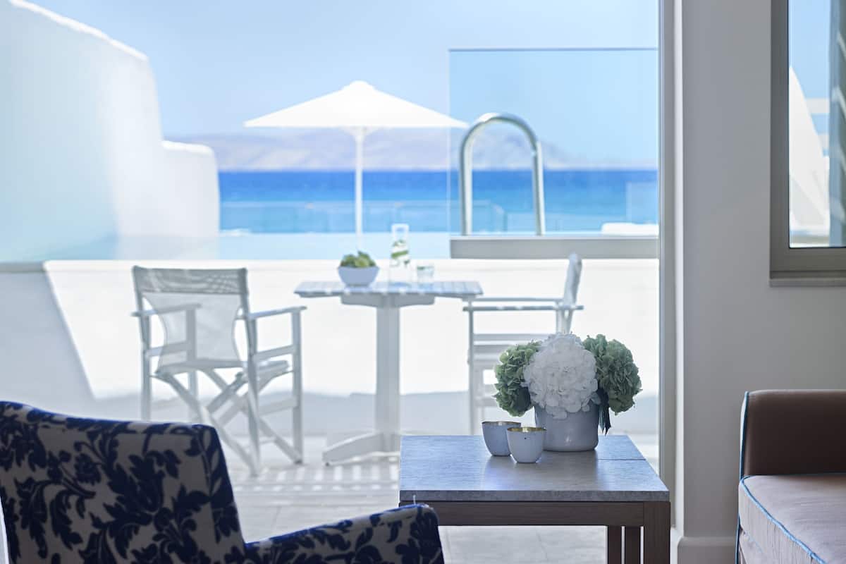 Ein Zimmer mit Meerblick, ein Tisch mit Blumen in einer Vase und ein Sessel.
