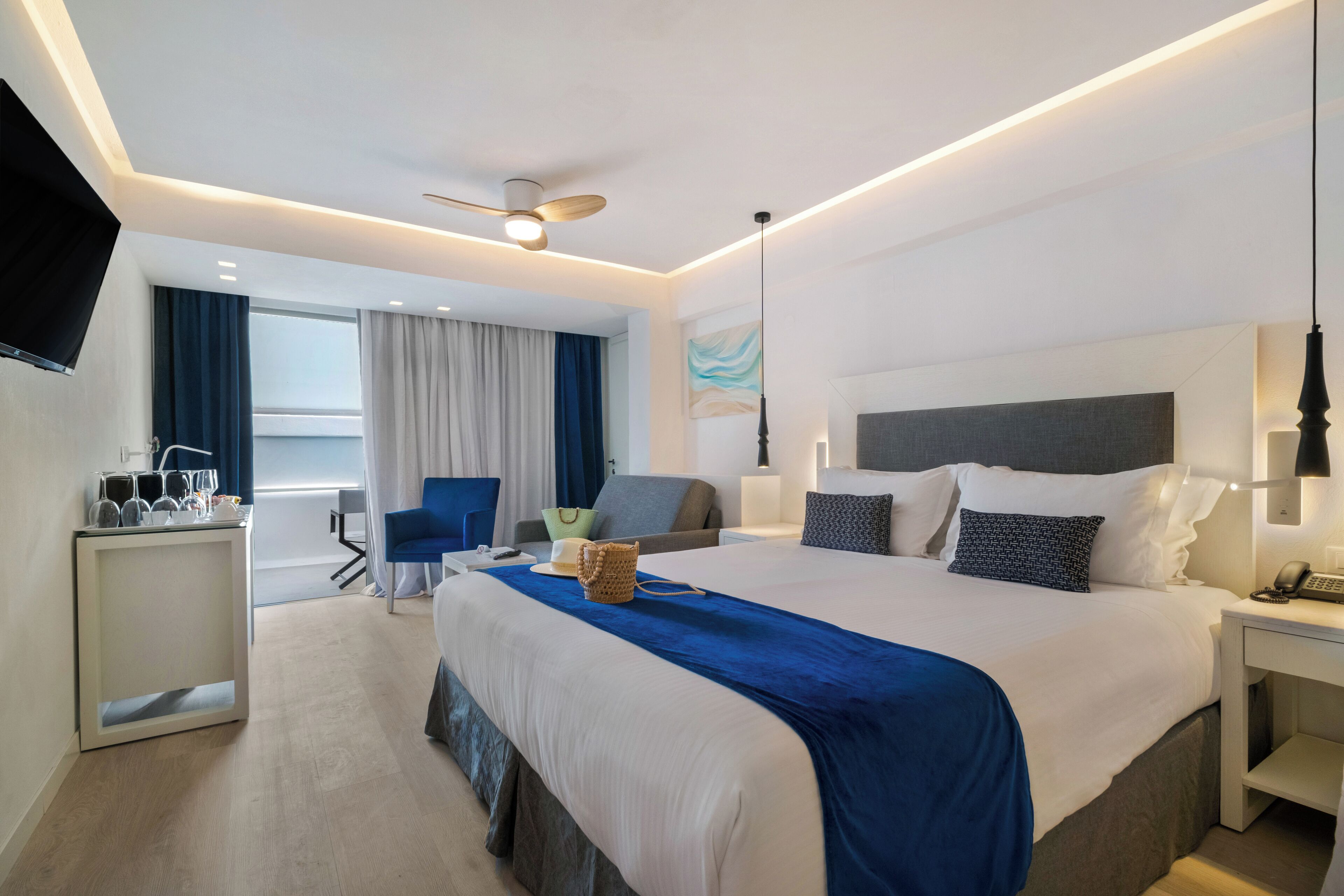 A modern hotel room with a large bed, a desk, a chair, and a TV mounted on the wall.