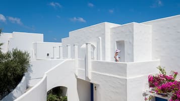 Un edificio blanco con una puerta azul y un balcón con flores rosadas.