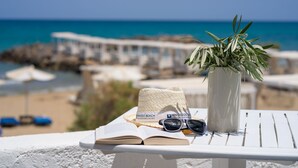 A beach view with a white table, a woven hat, sunglasses, and a potted plant.