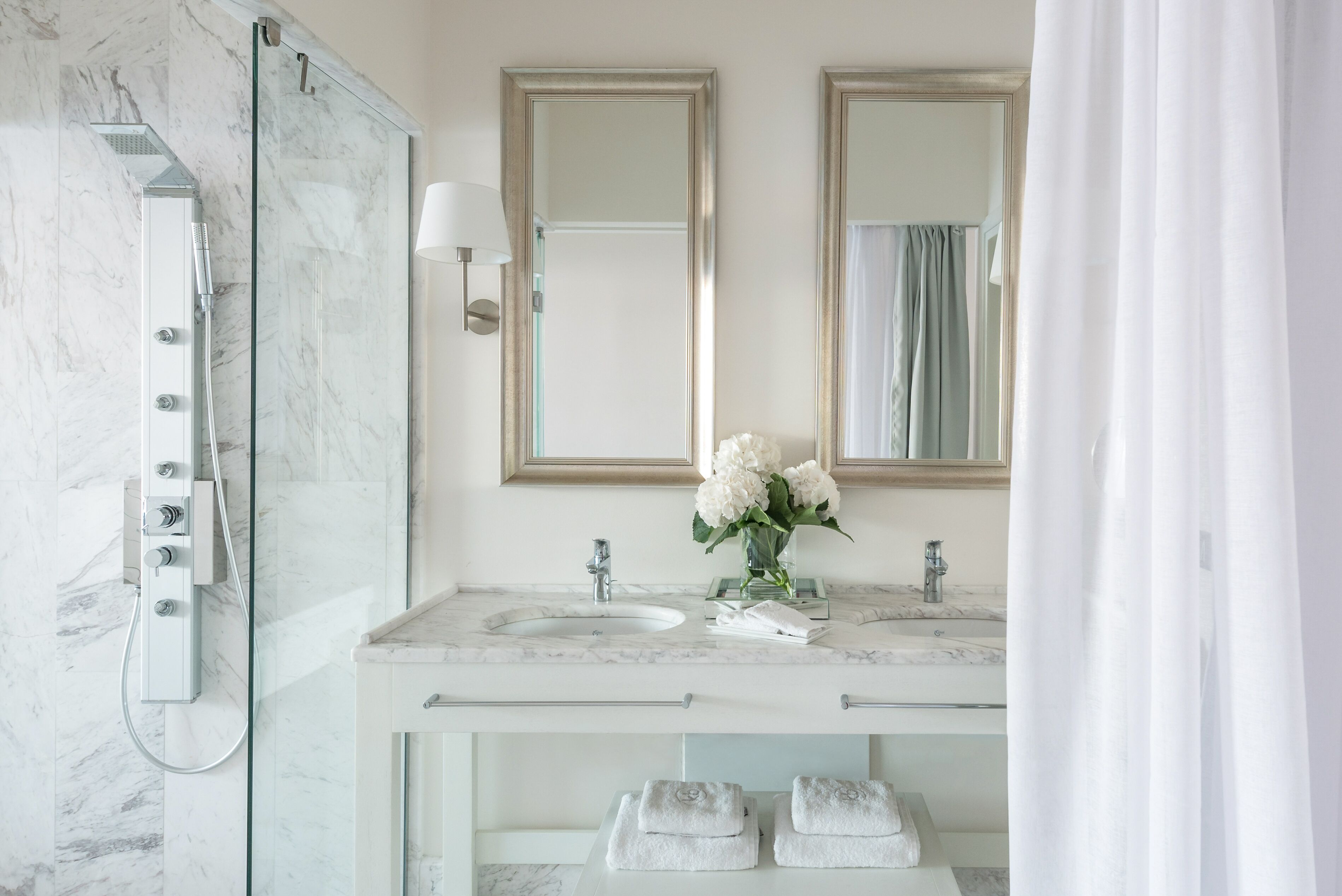 A modern bathroom with a glass-enclosed shower, two sinks, and a vanity with towels.
