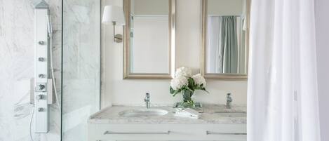 A modern bathroom with a glass-enclosed shower, two sinks, and a vanity with towels.