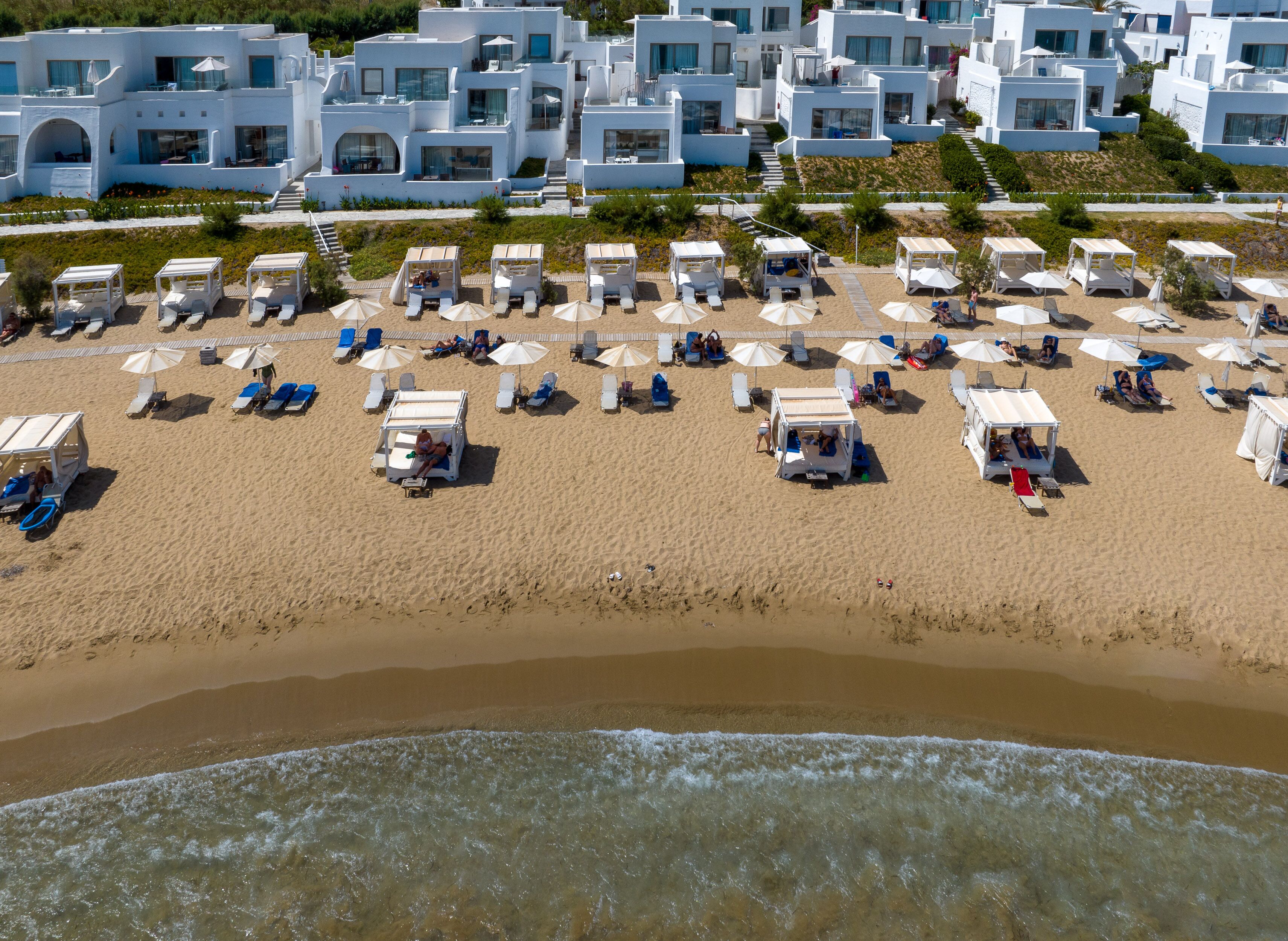 A beach with white buildings in the background, sun loungers, and umbrellas.