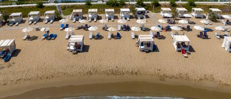 A beach with white buildings in the background, sun loungers, and umbrellas.
