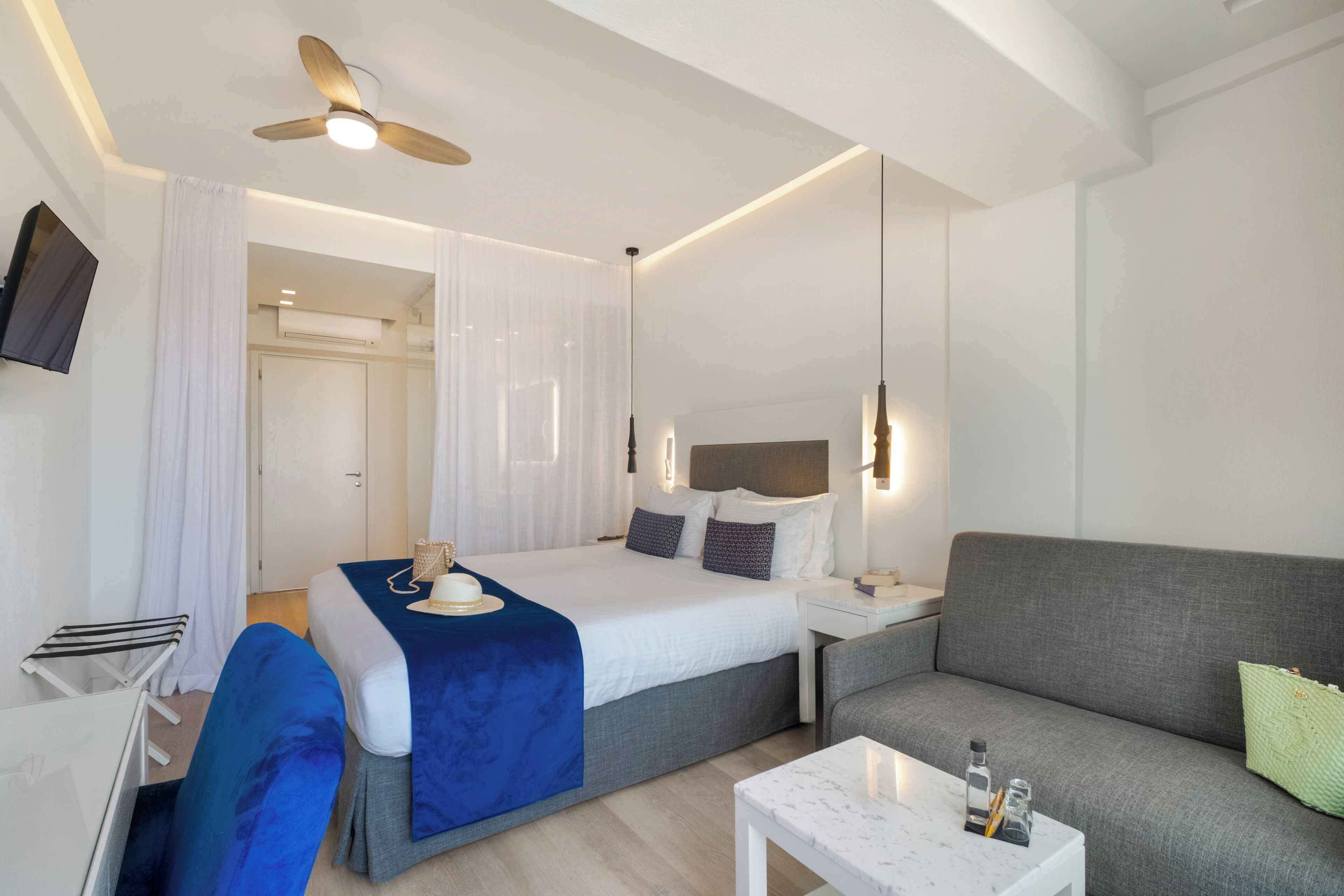 Une chambre d’hôtel moderne équipée d’un lit, d’un canapé, d’une petite table et d’un ventilateur de plafond.