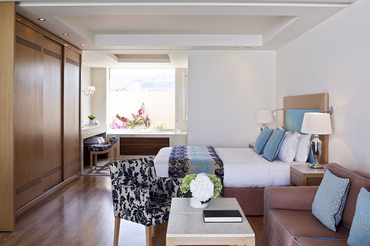 Ein modernes Hotelzimmer mit einem Bett, einer Couch und einem kleinen Tisch mit einem Buch und Blumen.