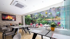 A modern dining area with a fireplace, comfortable seating, and a view of a lush indoor garden. - Beyond Hotel - Boutique Class - Special Class (Izmir)