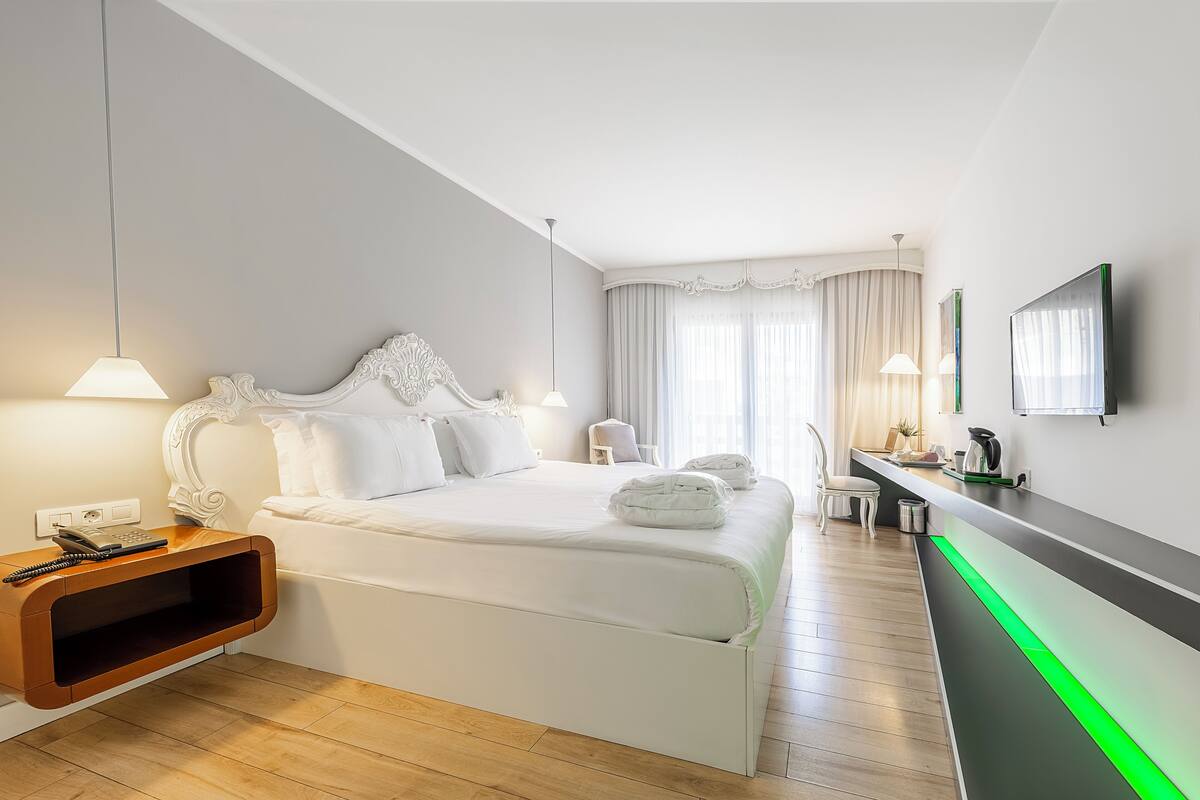 A modern hotel room with a large bed, bedside tables, a desk, and a television.
