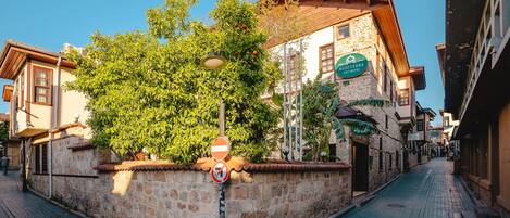 A narrow cobblestone street lined with traditional stone buildings, a tree with ripe fruit, and a sign for a local restaurant.