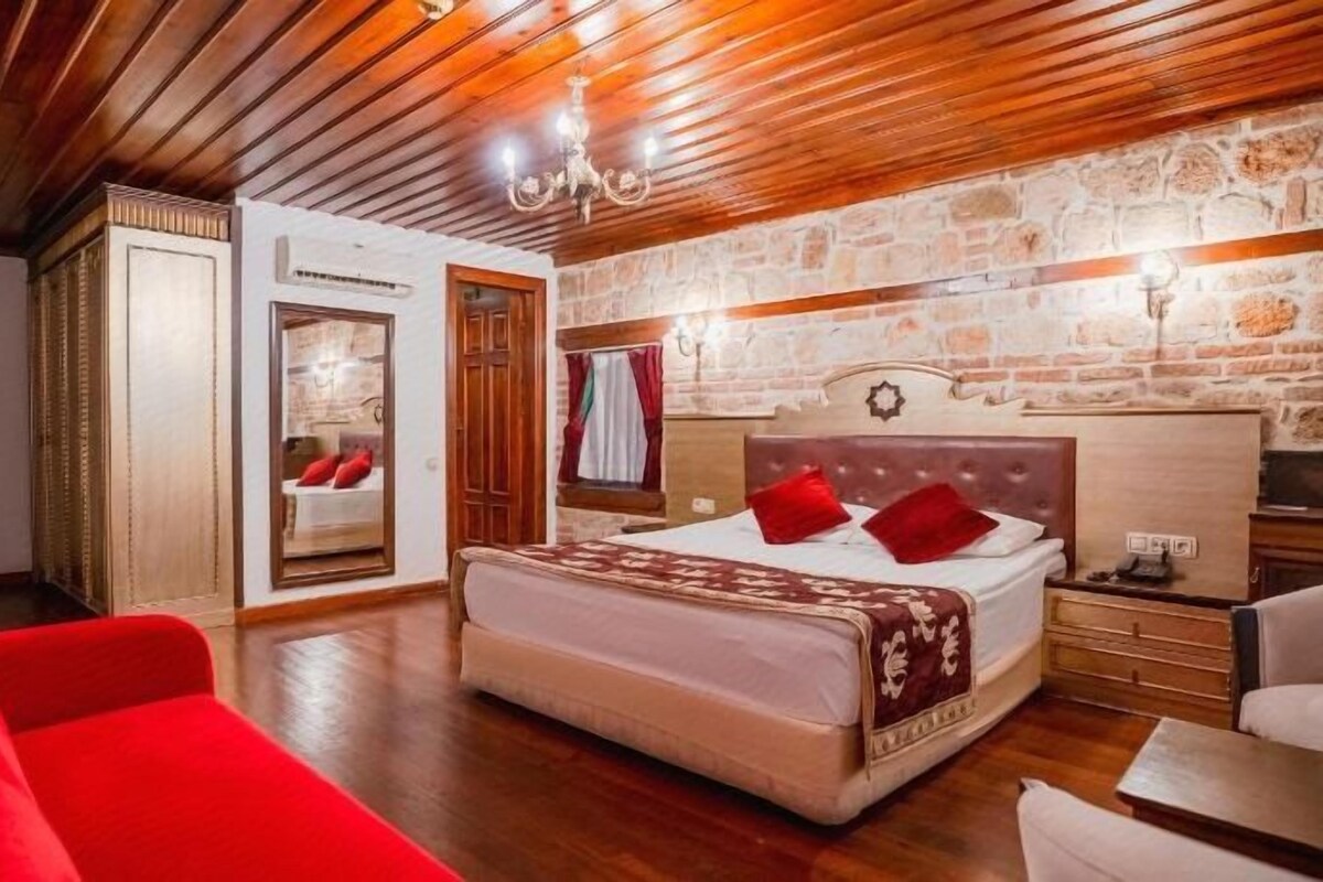 Une chambre avec un grand lit, un plafond en bois, un mur en pierre et un canapé rouge.