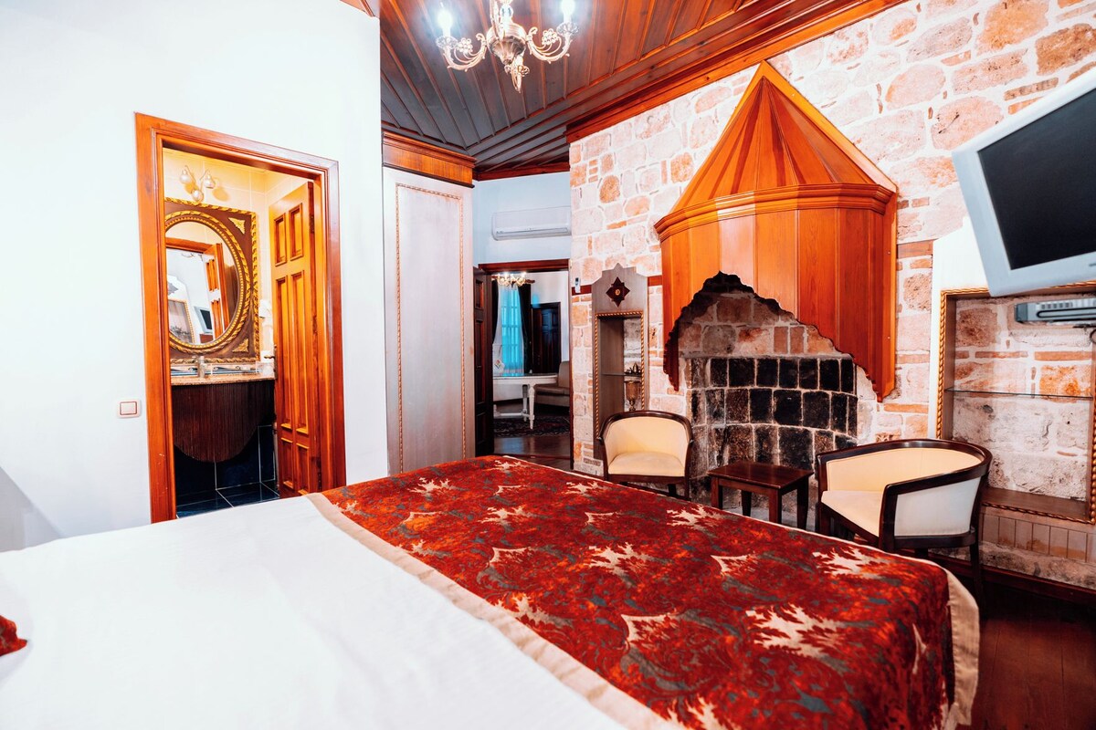 Une chambre d’hôtel avec un lit, deux fauteuils, une cheminée et un mur en pierre.