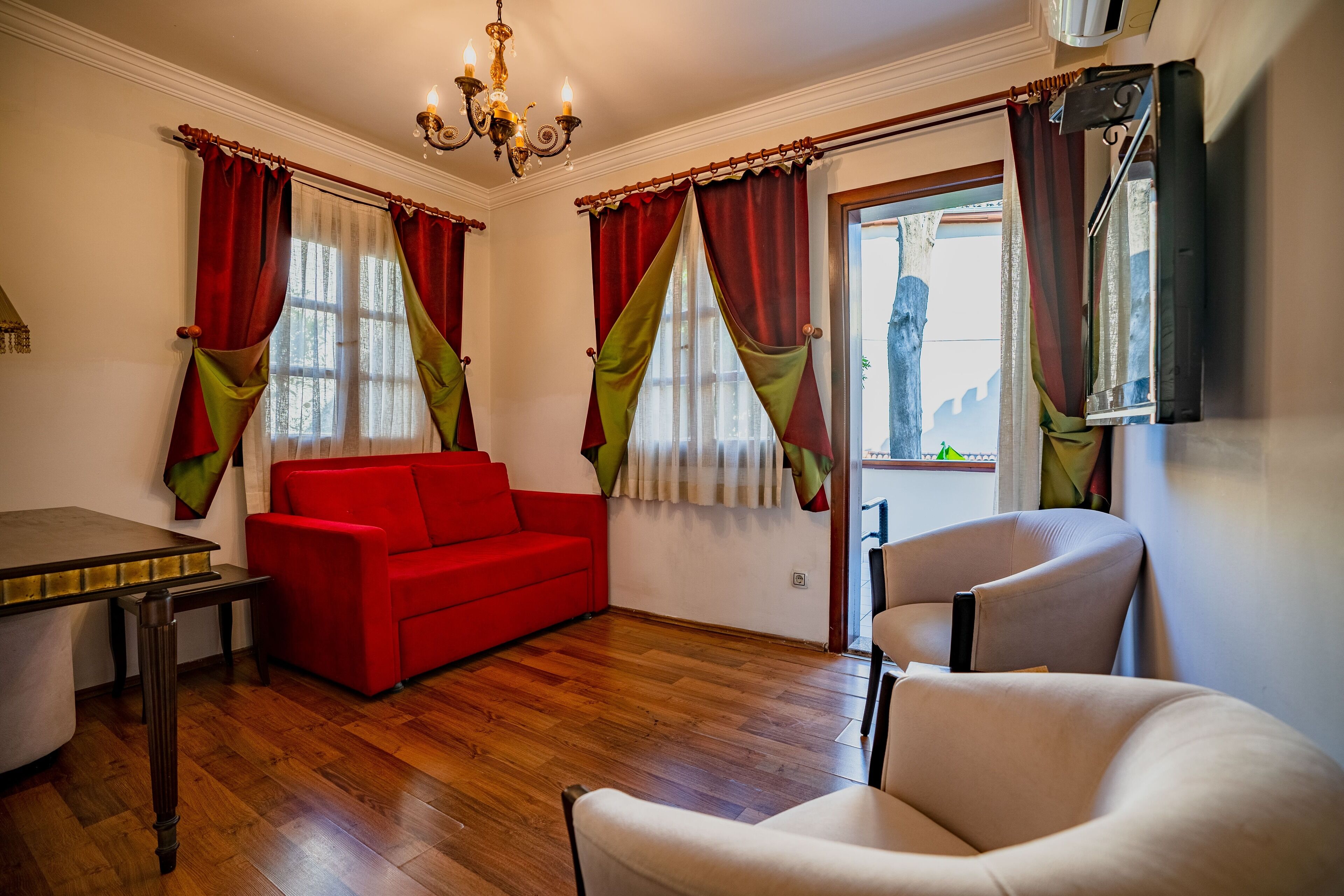 A living room with a red sofa, a beige armchair, a wooden table, and a chandelier.