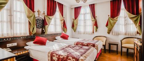 Habitación de hotel con dos camas, suelo de madera, candelabro y cortinas rojas y doradas.