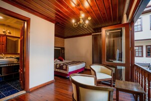 Habitación de hotel con techo de madera, cama con colcha roja y blanca, zona de estar con sillas y un espejo grande.