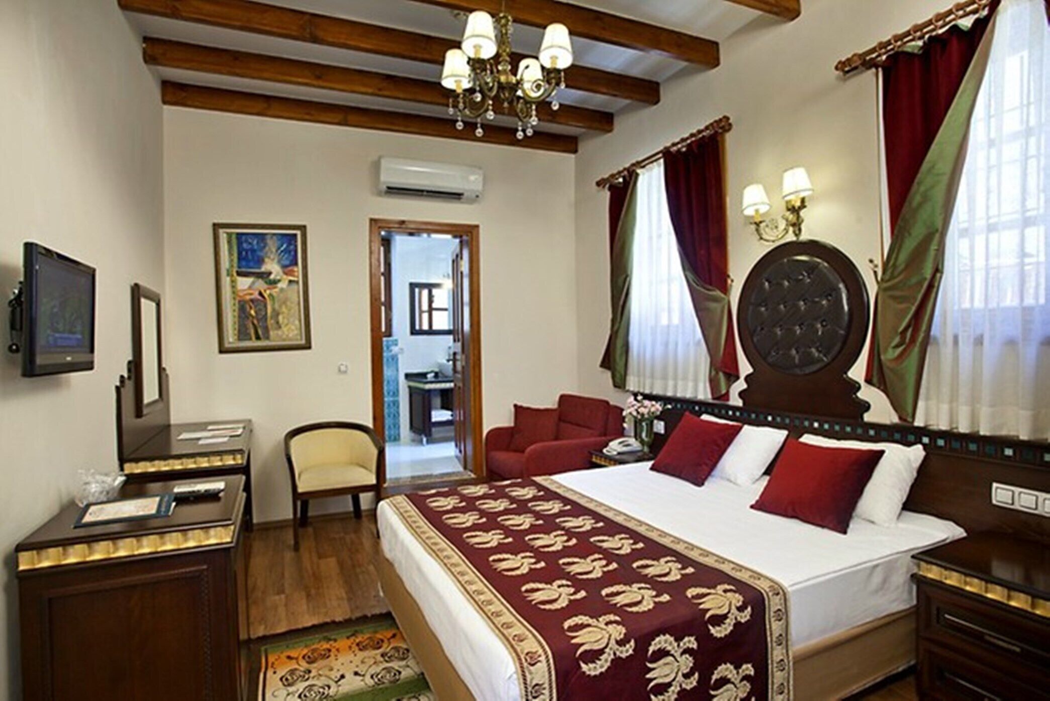 Een hotelkamer met een groot bed, een bureau, een stoel, een televisie en een schilderij aan de muur.
