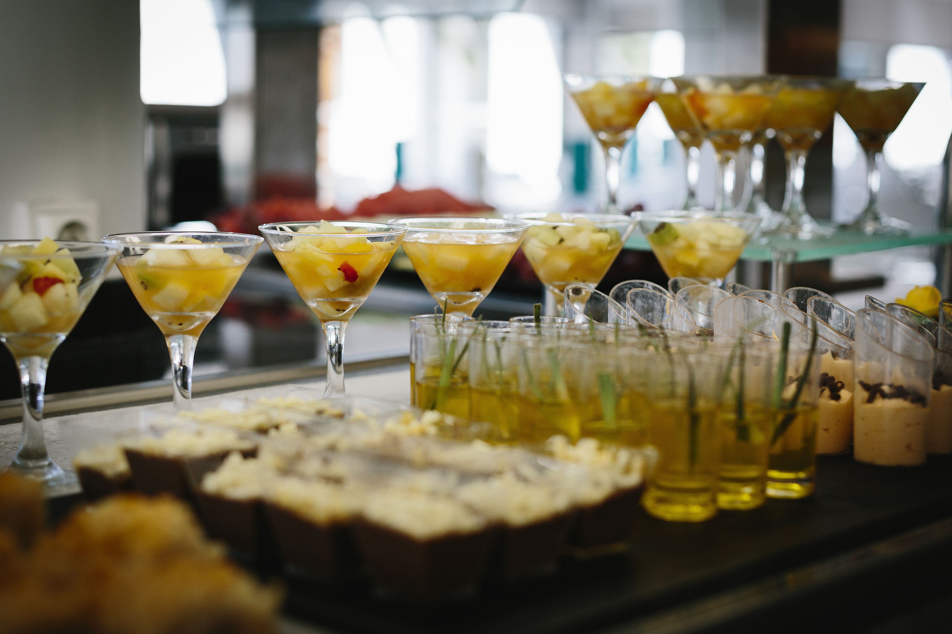 Un buffet proposant une variété de plats et de boissons, notamment des cocktails de fruits servis dans des verres à martini et d’autres boissons dans de petits gobelets.