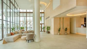 Un vestíbulo amplio con diseño moderno, que incluye una zona de estar con sofás y sillones, ventanas grandes y plantas en macetas.