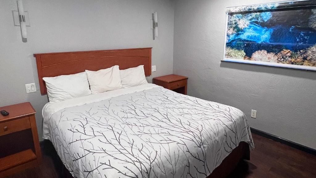 A bedroom with a bed, two nightstands, a wall-mounted TV, and a painting.